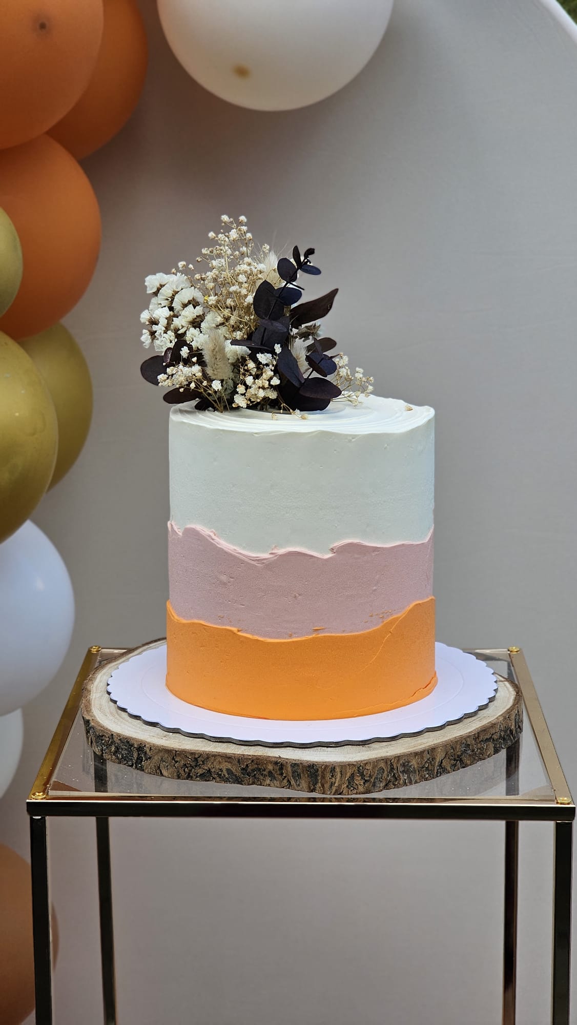 Tarta artesanal de buttercream en tres tonos —blanco, rosa y naranja— coronada con flores secas